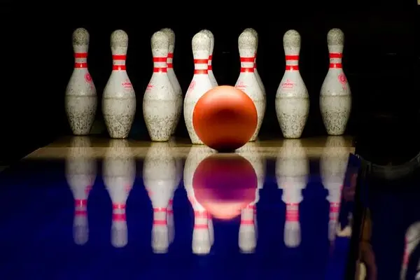 12 quilles de bowling blanches et rouges, avec une balle rouge devant.