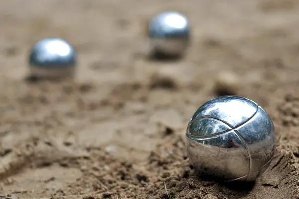 Trois boules de pétanque, dont 2 floues en arrière plan, sur du sable.