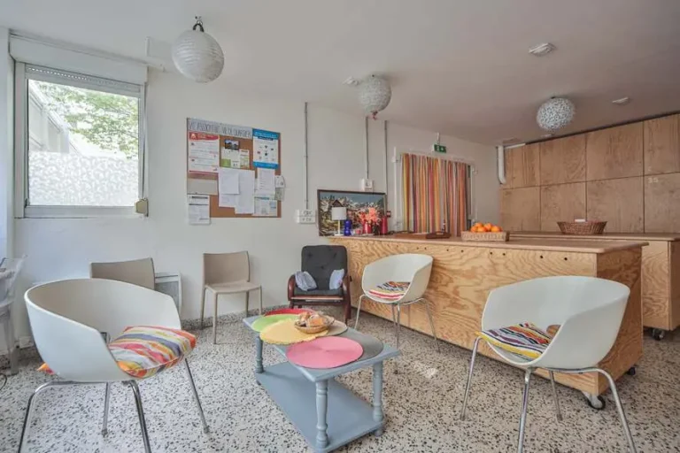 Photo du salon de la bagagerie. On y voit des fauteuils autour d'une table basse où est posée une corbeille qui contient des viennoiseries. Au fond à gauche, la fenêtre sur cours, et à droite, une partie des casiers des accueillis.
